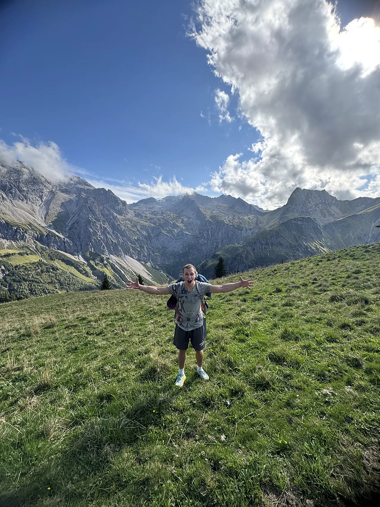 Mit ausgebreiteten Armen auf einer Almwiese vor schroffen Bergen