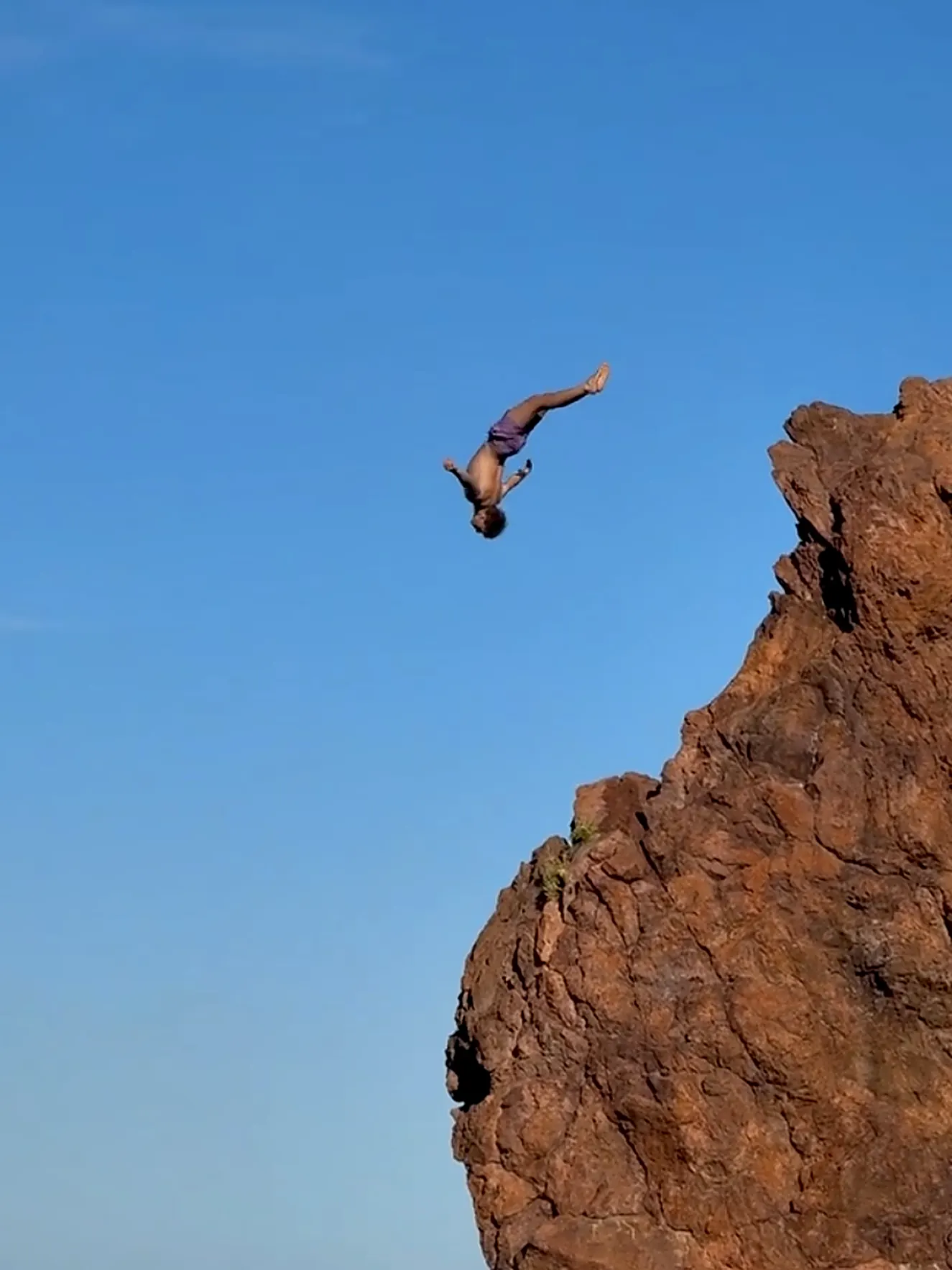 Backflip von einer roten Klippe in den blauen Himmel