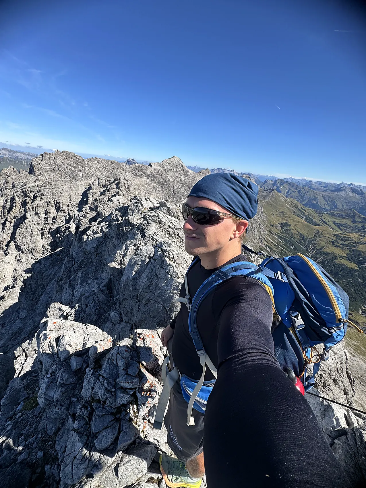 Clemens mit Rucksack und Sonnenbrille auf einem Felsgrat in den Alpen