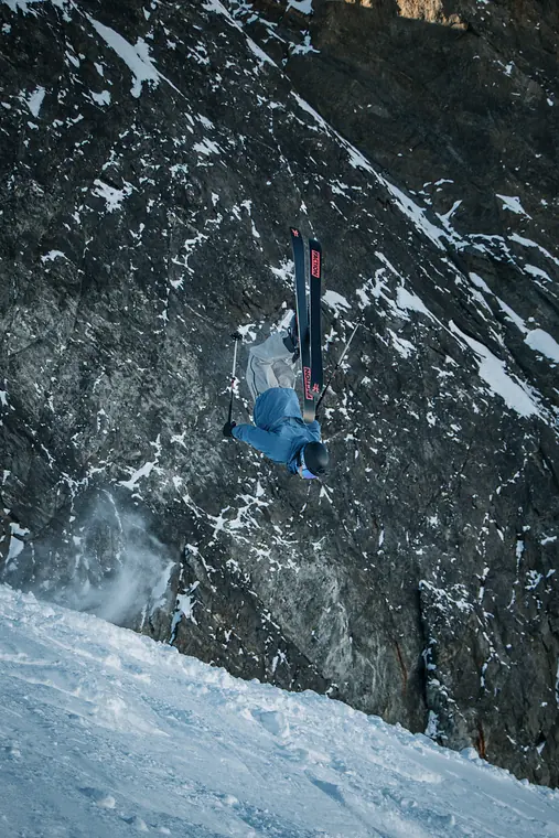 Backflip auf Ski vor einer verschneiten Felswand